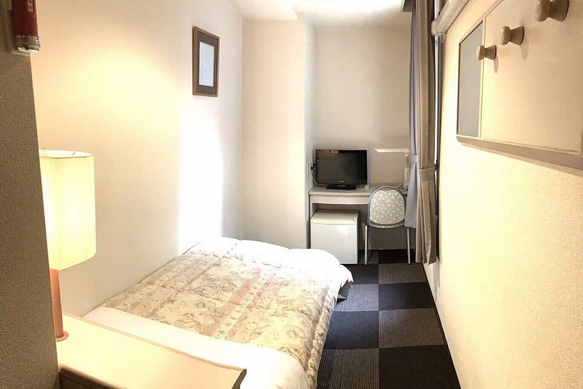 Une chambre d’hôtel avec un lit, un bureau équipé d’un ordinateur, une chaise et une lampe.