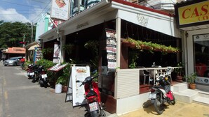 Un caffè con un cartello pubblicitario che offre bistecca e cucina tailandese, e una motocicletta parcheggiata davanti.