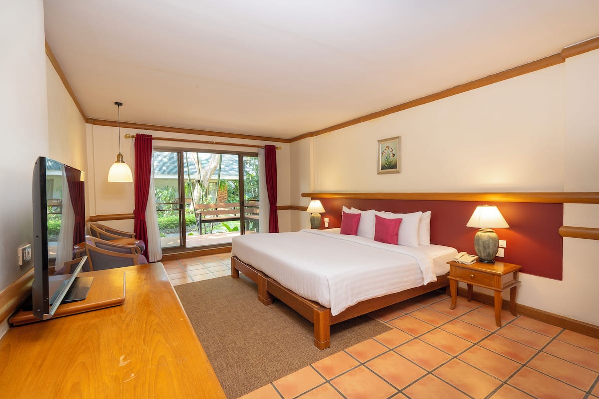 Habitación de hotel con cama, mesitas de noche, un escritorio con una computadora portátil, televisor y vistas al exterior.