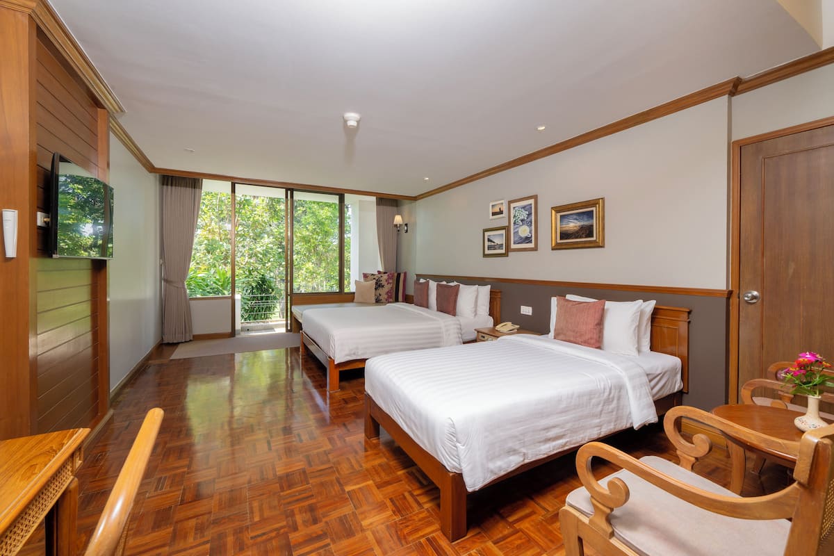 Habitación de hotel con dos camas, suelo de madera, televisión y ventana con vistas a zonas verdes.