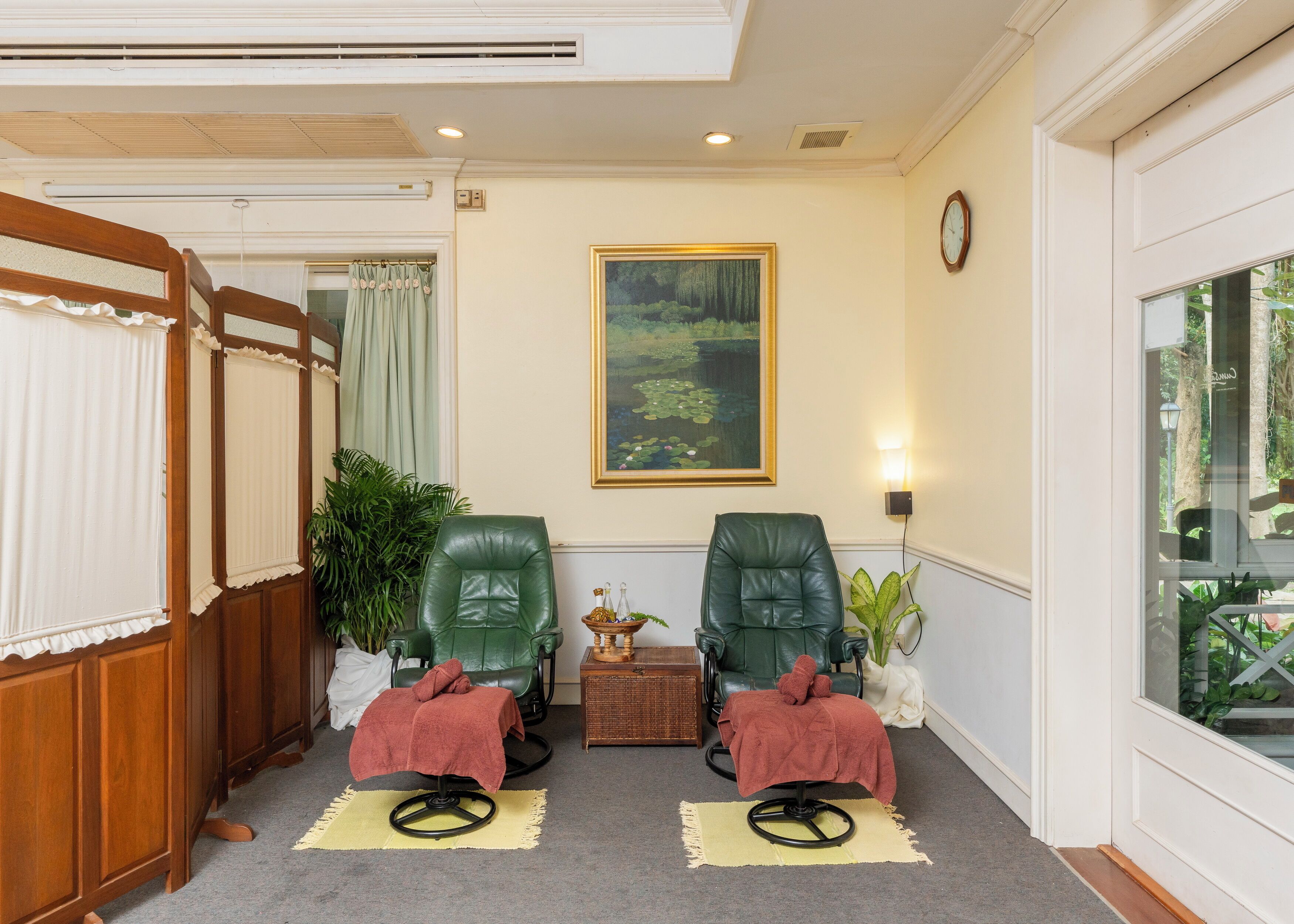 Una habitación con dos sillones de cuero verde, una mesita con una lámpara y un cuadro de un bosque en la pared.