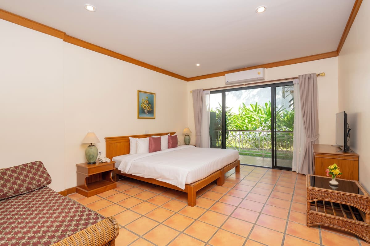 Una habitación de hotel con cama, sofá, televisión, mesa con florero y balcón con plantas.