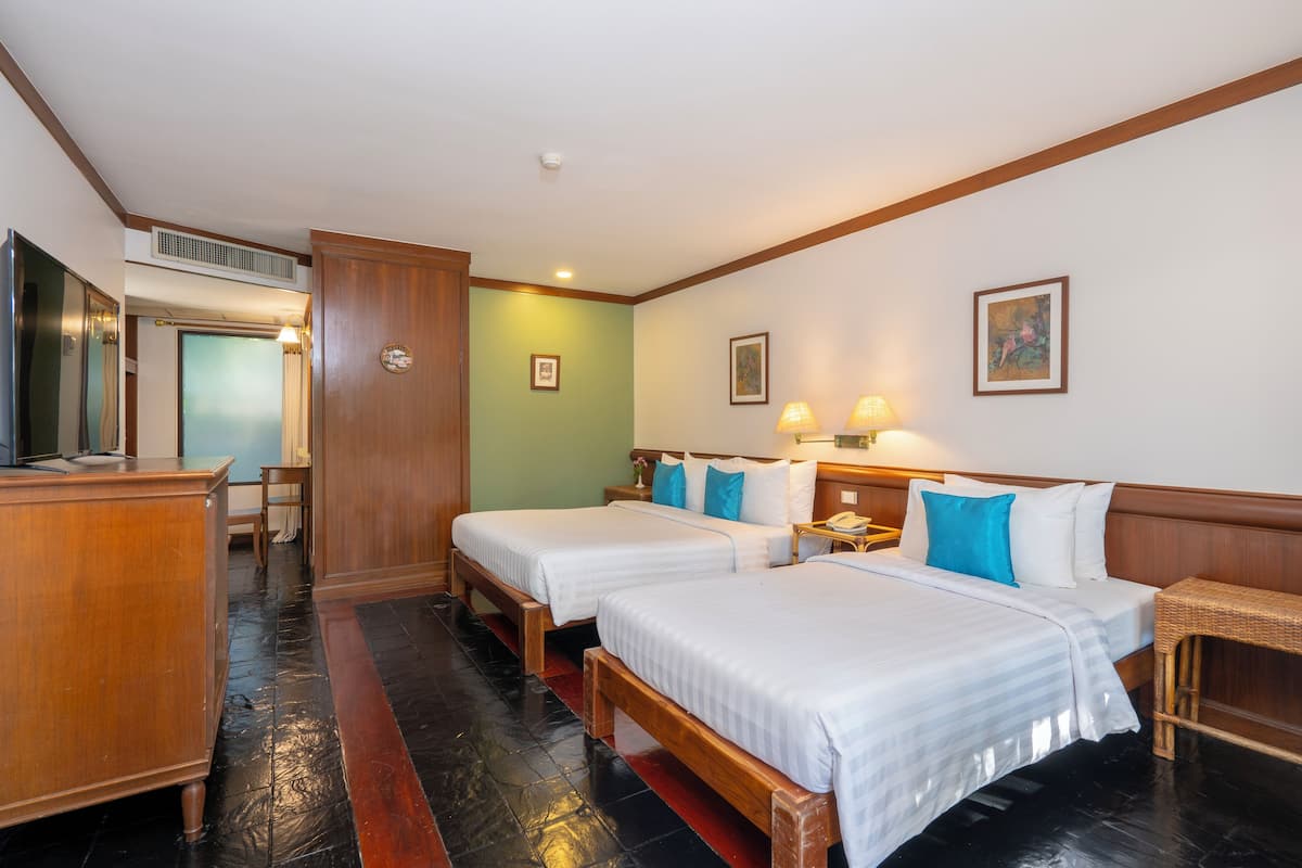 Habitación de hotel con dos camas, un escritorio de madera, una silla y una mesita con lámpara.