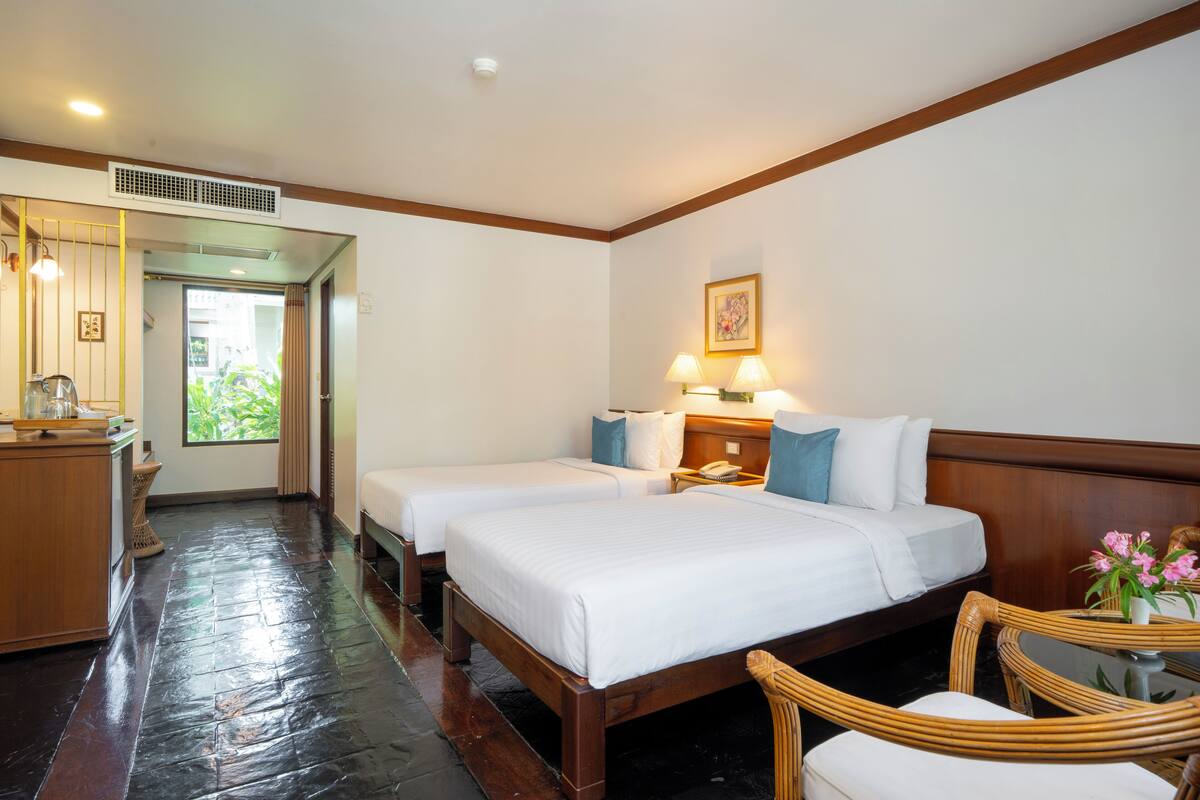 Habitación de hotel con dos camas, un escritorio de madera, una silla y una mesita con flores.