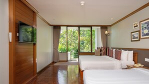 Habitación de hotel con dos camas, un televisor y un ventanal con vistas al verdor.