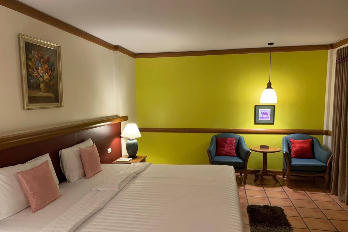 Habitación de hotel con cama, dos sillones, una mesita, lámpara, un cuadro y una lámpara del techo.