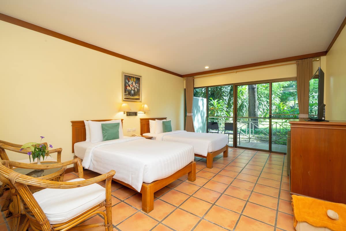 Habitación de hotel con dos camas, zona de estar con una silla, una mesa y vistas al exterior.