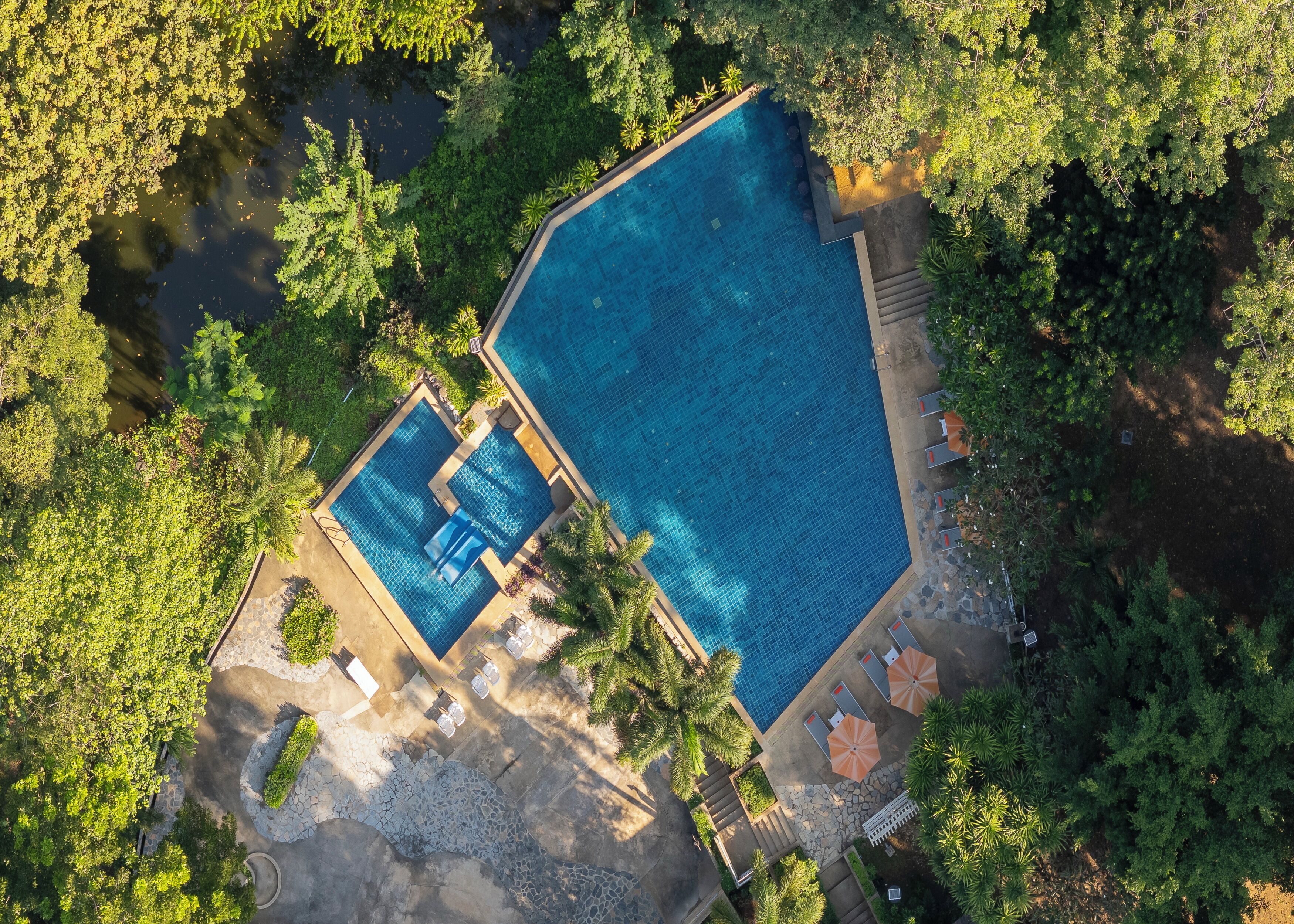An aerial view of a resort with two swimming pools surrounded by lush greenery and palm trees.
