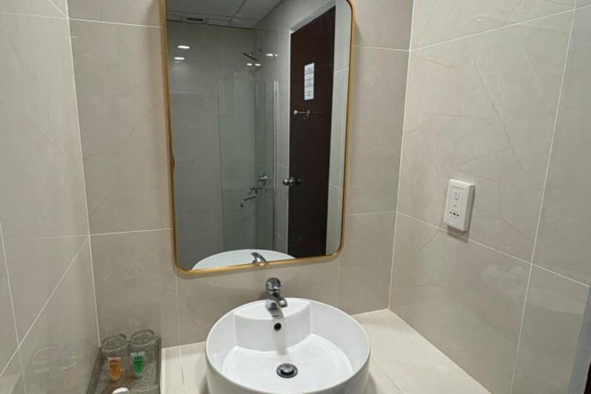 A bathroom with a round sink, a mirror with a wooden frame, and a shower visible in the background.