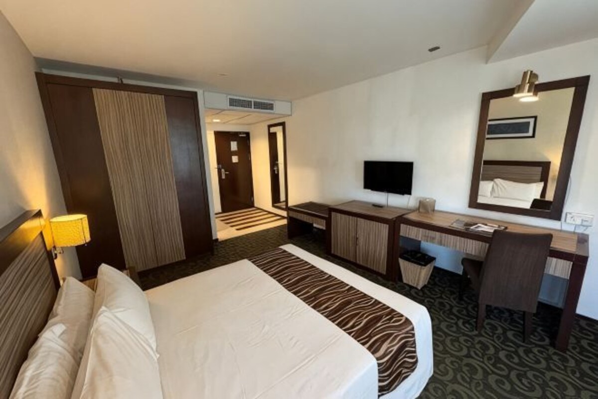A hotel room with a bed, desk, television, and a mirror.