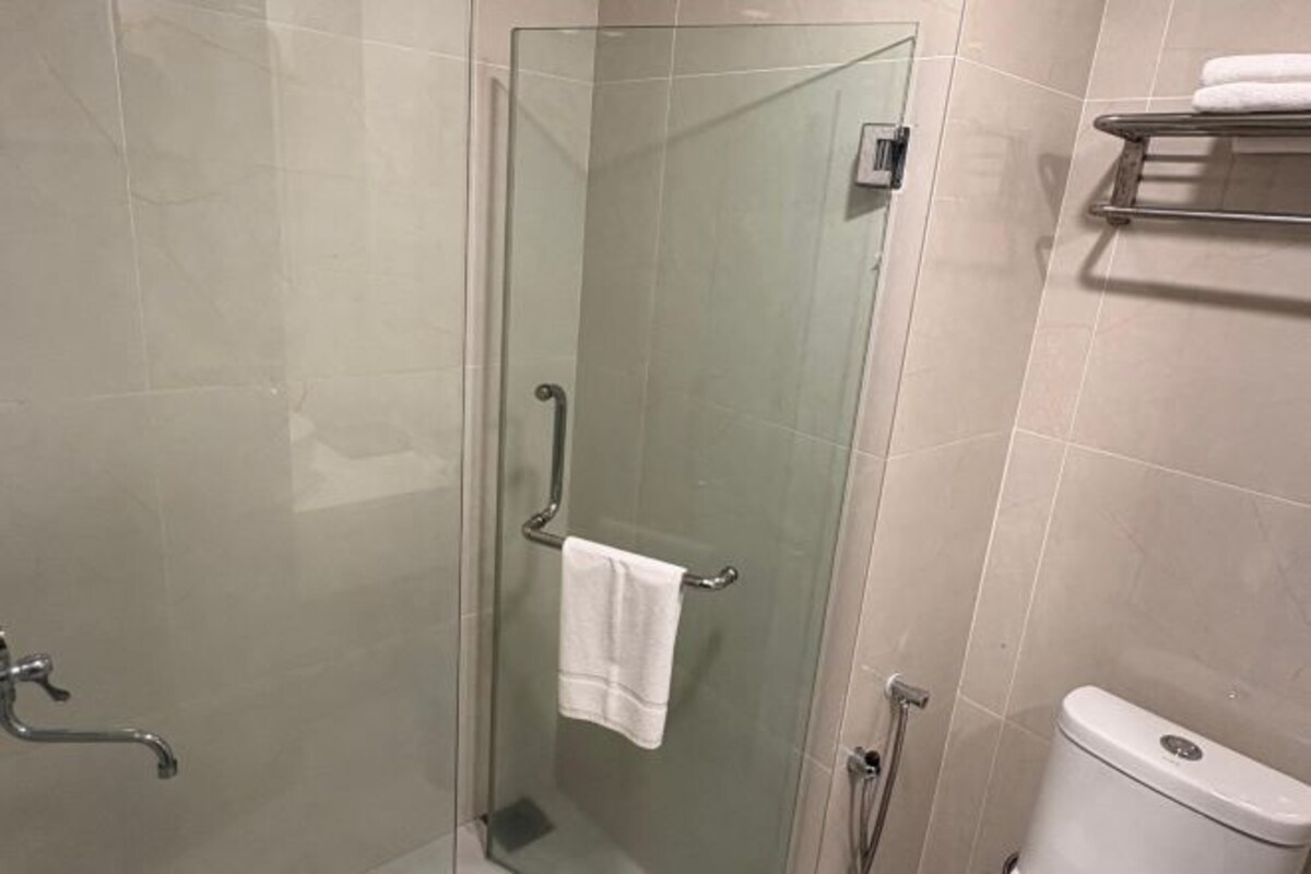 A glass-enclosed shower stall with a towel hanging on a metal handle, a white toilet, and a metal towel rack on the wall.