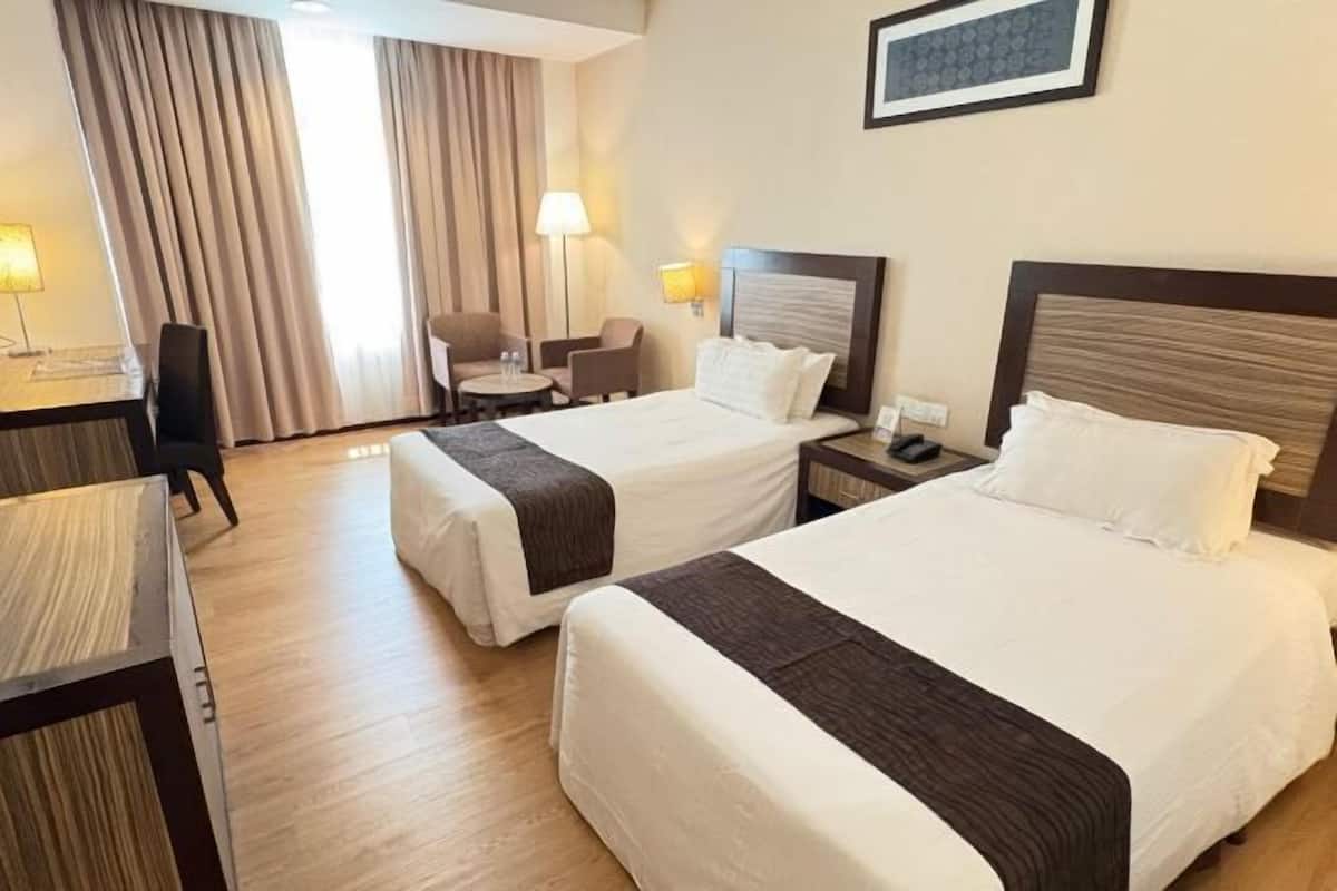 Une chambre d’hôtel avec deux lits, un bureau, une chaise et une lampe.