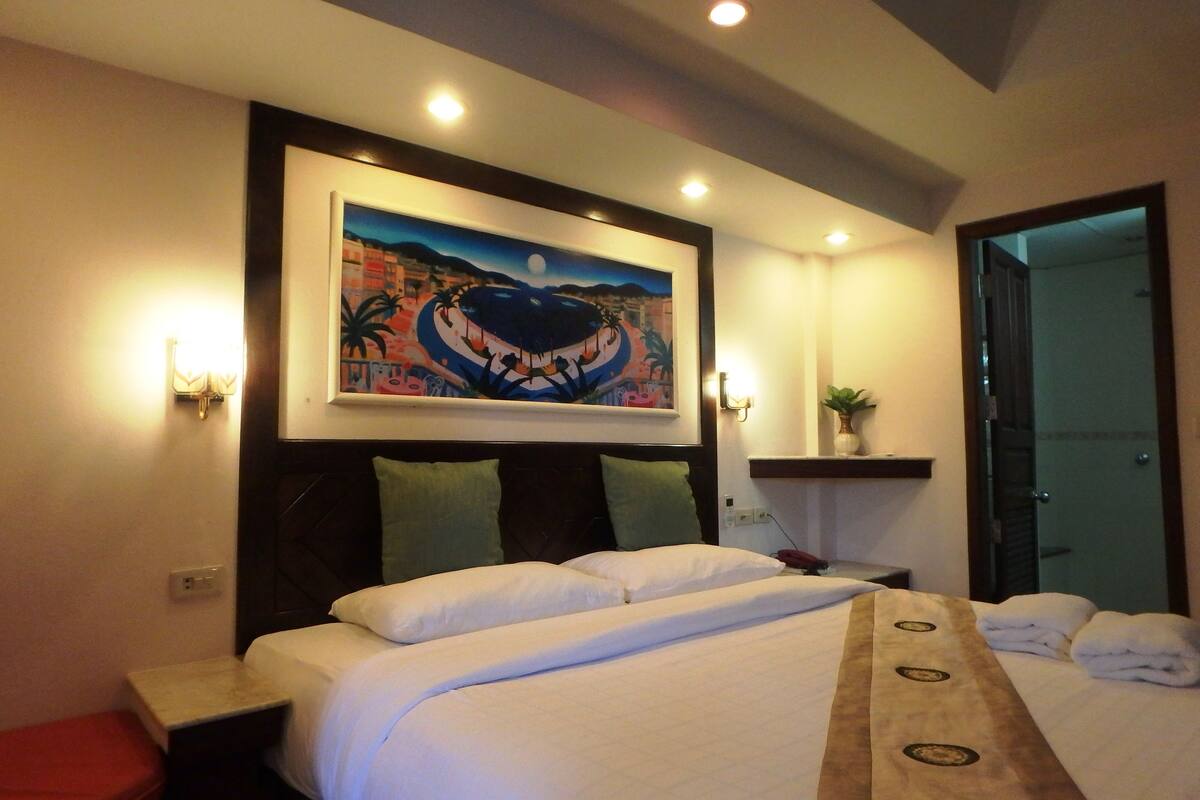 A hotel room with a bed, a nightstand, a red chair, a painting on the wall, and a door.