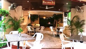 A restaurant with outdoor seating, white chairs, and tables, surrounded by potted plants. - Paradise Inn (Karon)