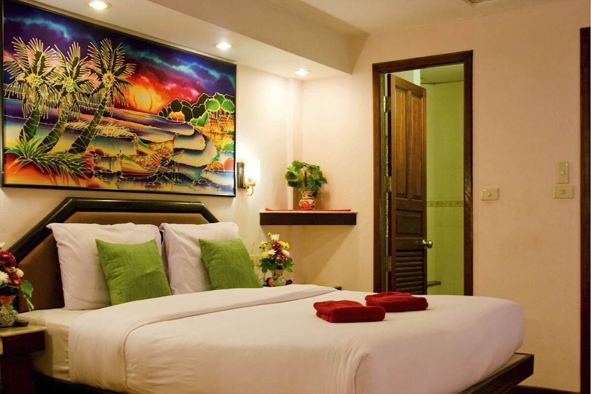 A hotel room with a bed, pillows, a painting, a vase with flowers, and a door.
