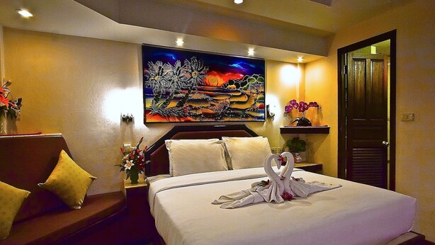 A hotel room with a bed, a painting on the wall, and a door. - Paradise Inn (Karon)