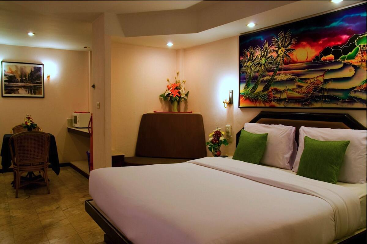 A hotel room with a large bed, a desk with a chair, a painting on the wall, and a window with a view.