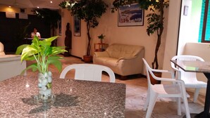 A room with a marble table, white chairs, a beige sofa, and potted plants. - Paradise Inn (Karon)