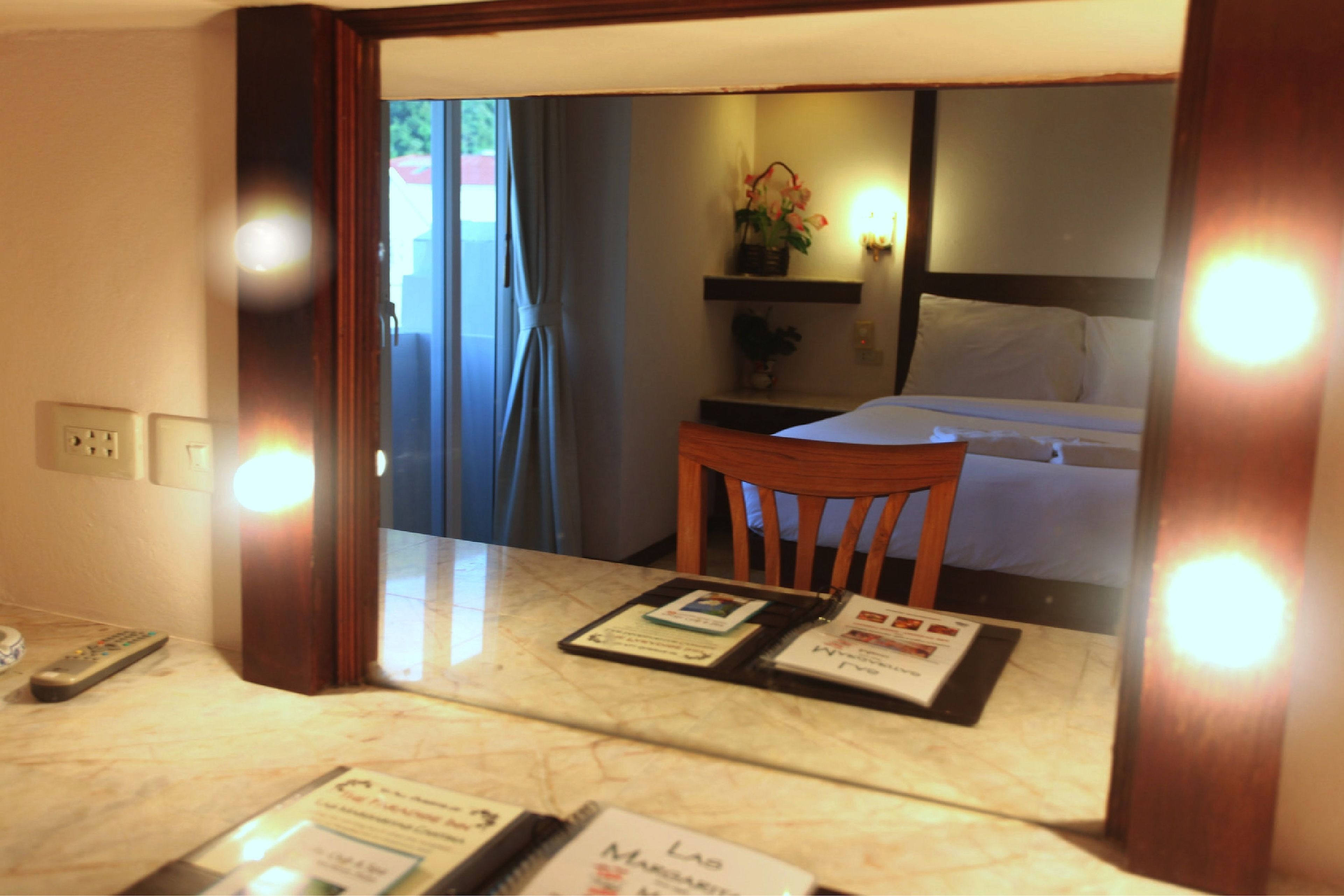 A hotel room with a bed, a chair, a table with brochures, and a window with curtains.