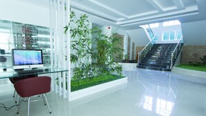 A modern interior with a glass desk, computer, red chair, and a green plant arrangement. - Grand Seagull Hotel (Sihanoukville)