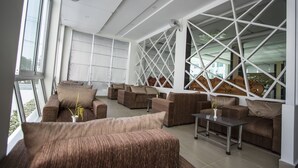 A spacious, modern living area with multiple sofas and a coffee table, large windows with a geometric design, and a view of the outdoors. - Grand Seagull Hotel (Sihanoukville)