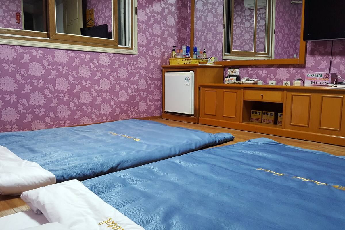 A hotel room with two beds, a small refrigerator, a wooden cabinet with toiletries, and a mirror.