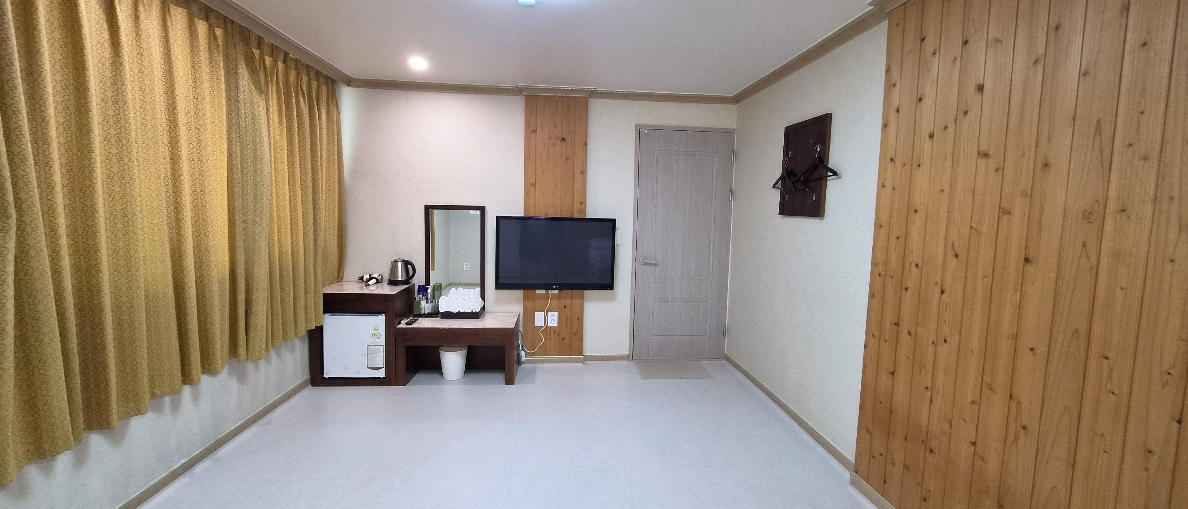 A hotel room with a wooden accent wall, a flat-screen TV, a vanity with a mirror, and a small kitchenette.