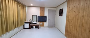A hotel room with a wooden accent wall, a flat-screen TV, a vanity with a mirror, and a small kitchenette.