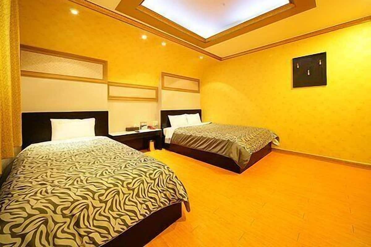 A hotel room with two beds, a skylight, and a small bedside table with a lamp.