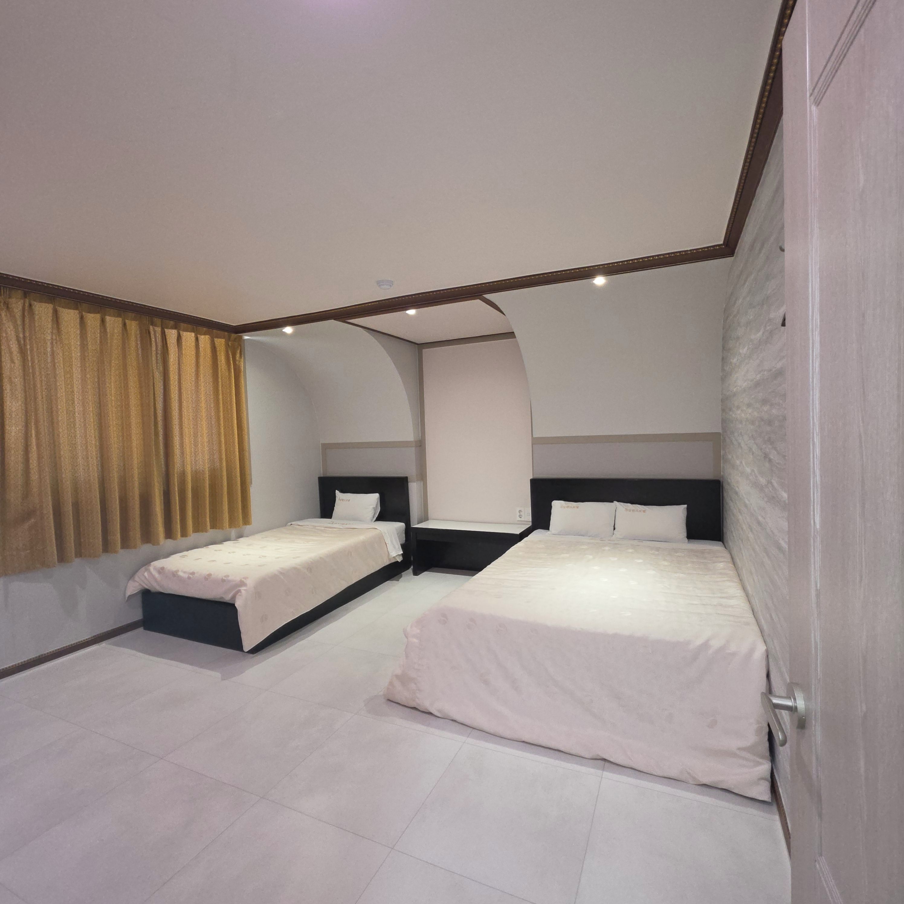 A hotel room with two beds, a curved ceiling, and a large window with curtains.
