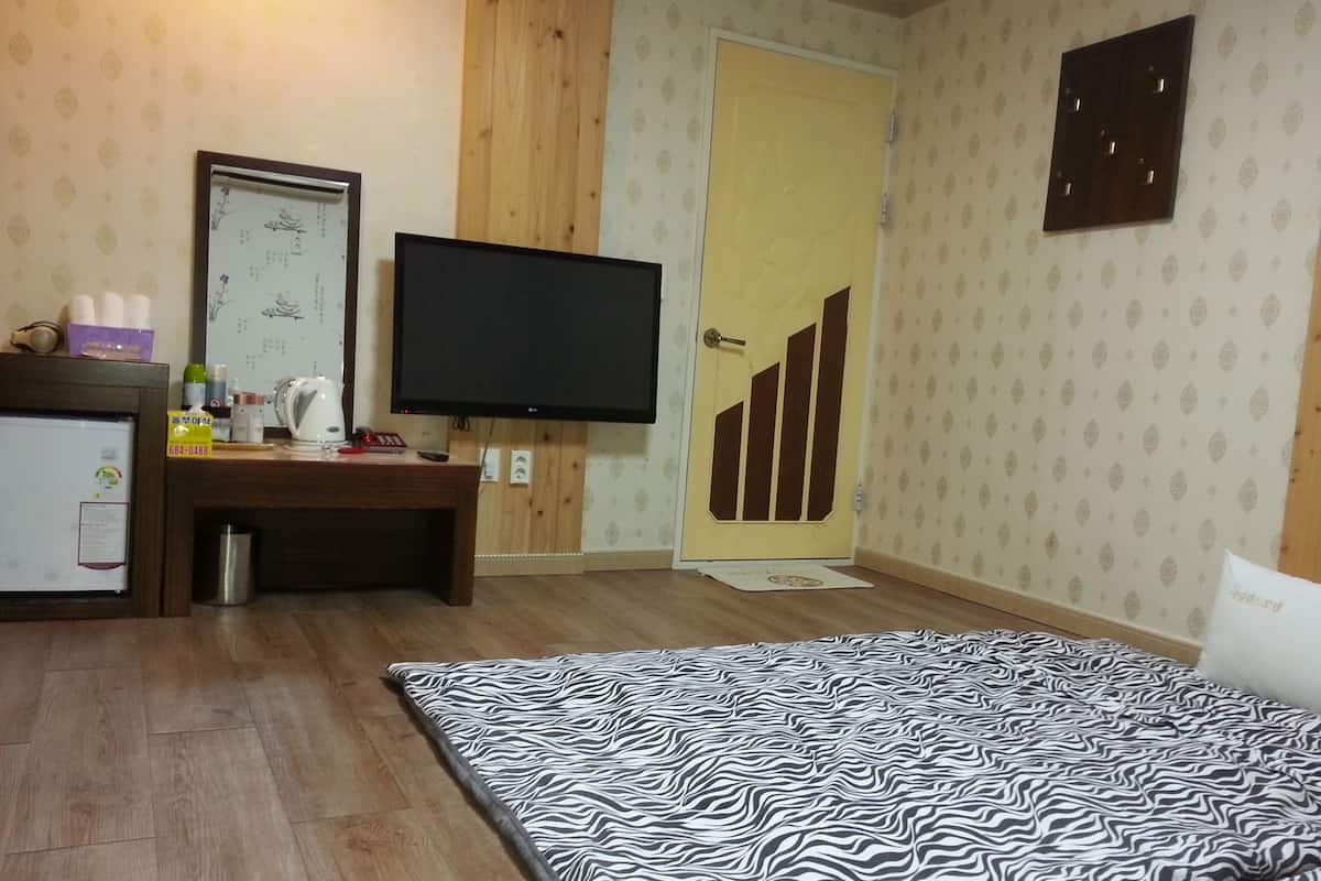 A hotel room with a bed, a desk with a computer, a television, and a door.