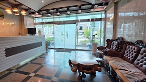 A reception area with a reception desk, a sofa, and a large window with a view of the street. - Island Motel (Yeosu)