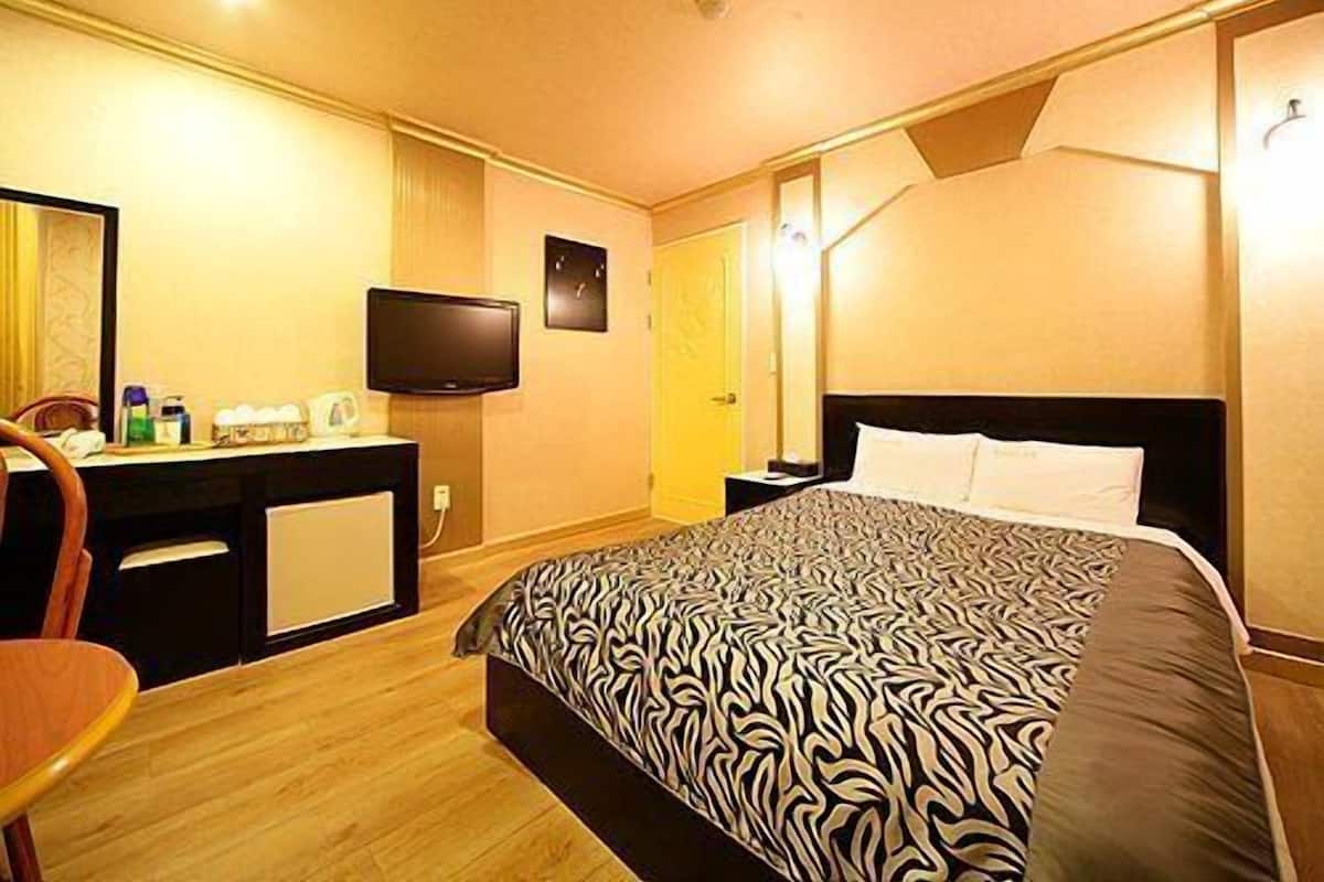A hotel room with a bed, a desk with a television, and a mirror.