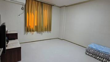 Een kamer met een plafondlamp, een airconditioning, een bureau met stoel en een bed met beddengoed met een patroon.