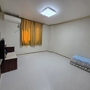 Una habitación con luz en el techo, aire acondicionado, un escritorio con silla y una cama con ropa de cama estampada.