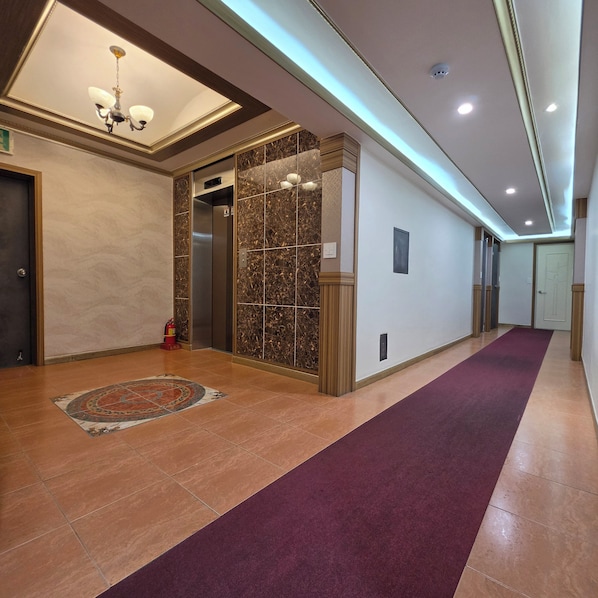 A hotel lobby with a marble wall, an elevator, a fire extinguisher, and a patterned rug.