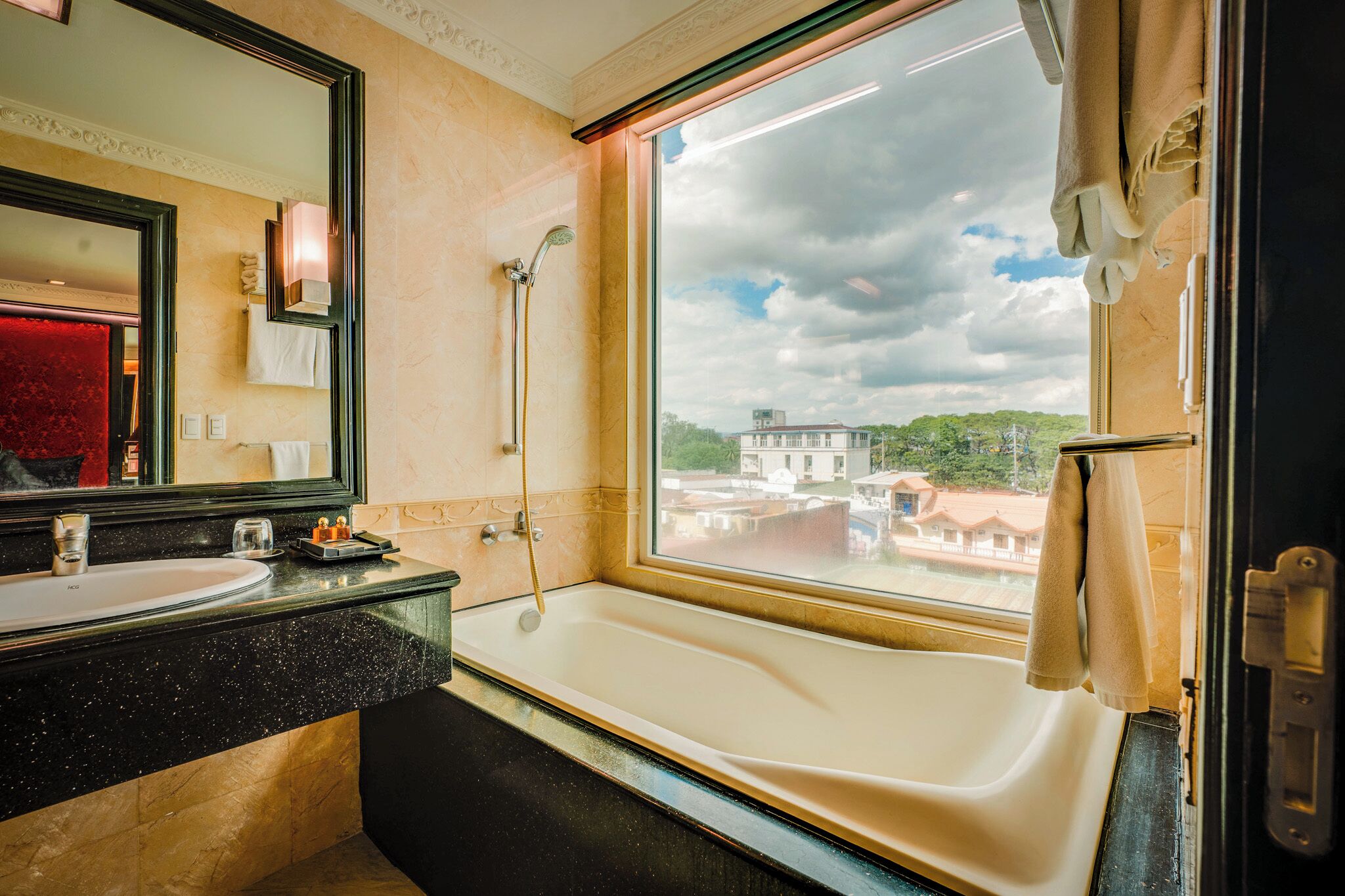 Un baño con una bañera grande, un lavabo y un espejo. Hay una ventana que ofrece vistas a edificios y árboles.