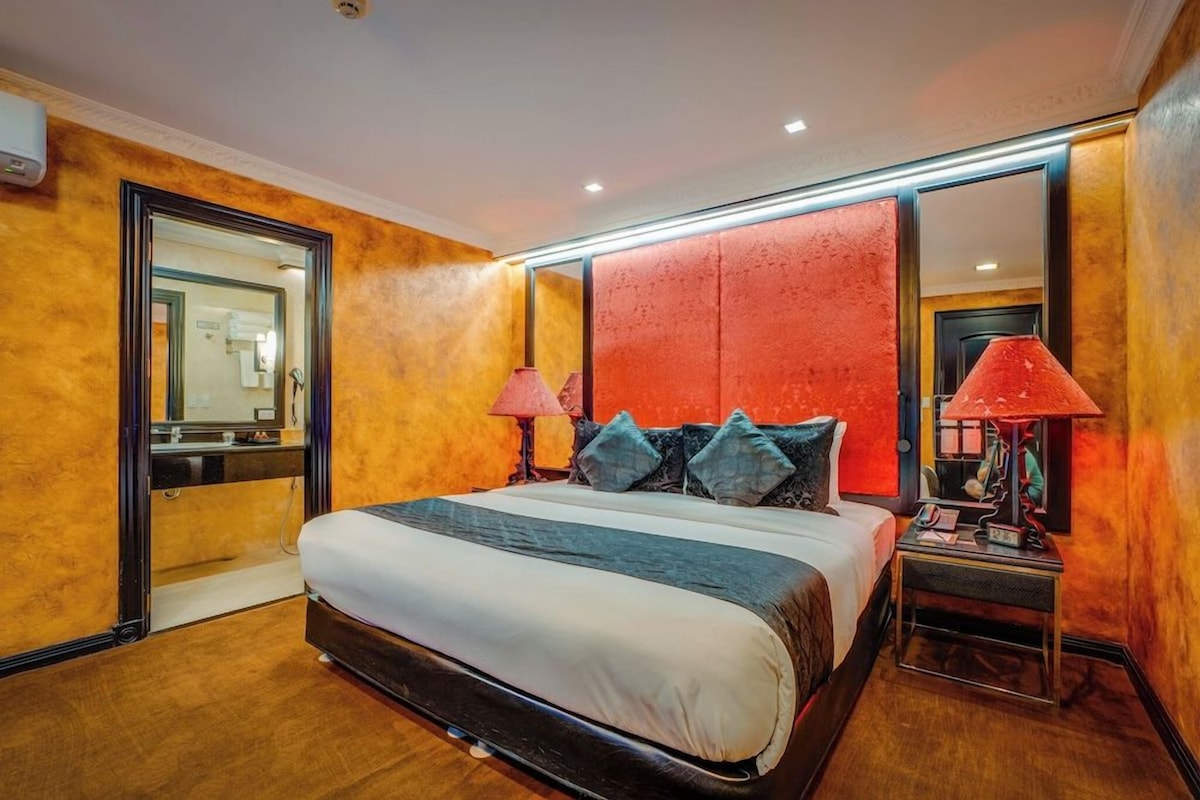 A hotel room with a large bed, bedside lamps, a mirror, and a door leading to a bathroom.