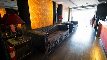 A lobby with a sofa, two lamps, a fire extinguisher, and a patterned wall.