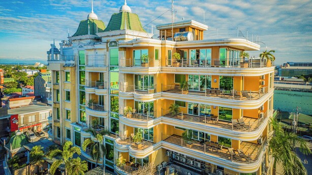 Un hotel de varios pisos con balcones, ventanas amplias y techo verde.