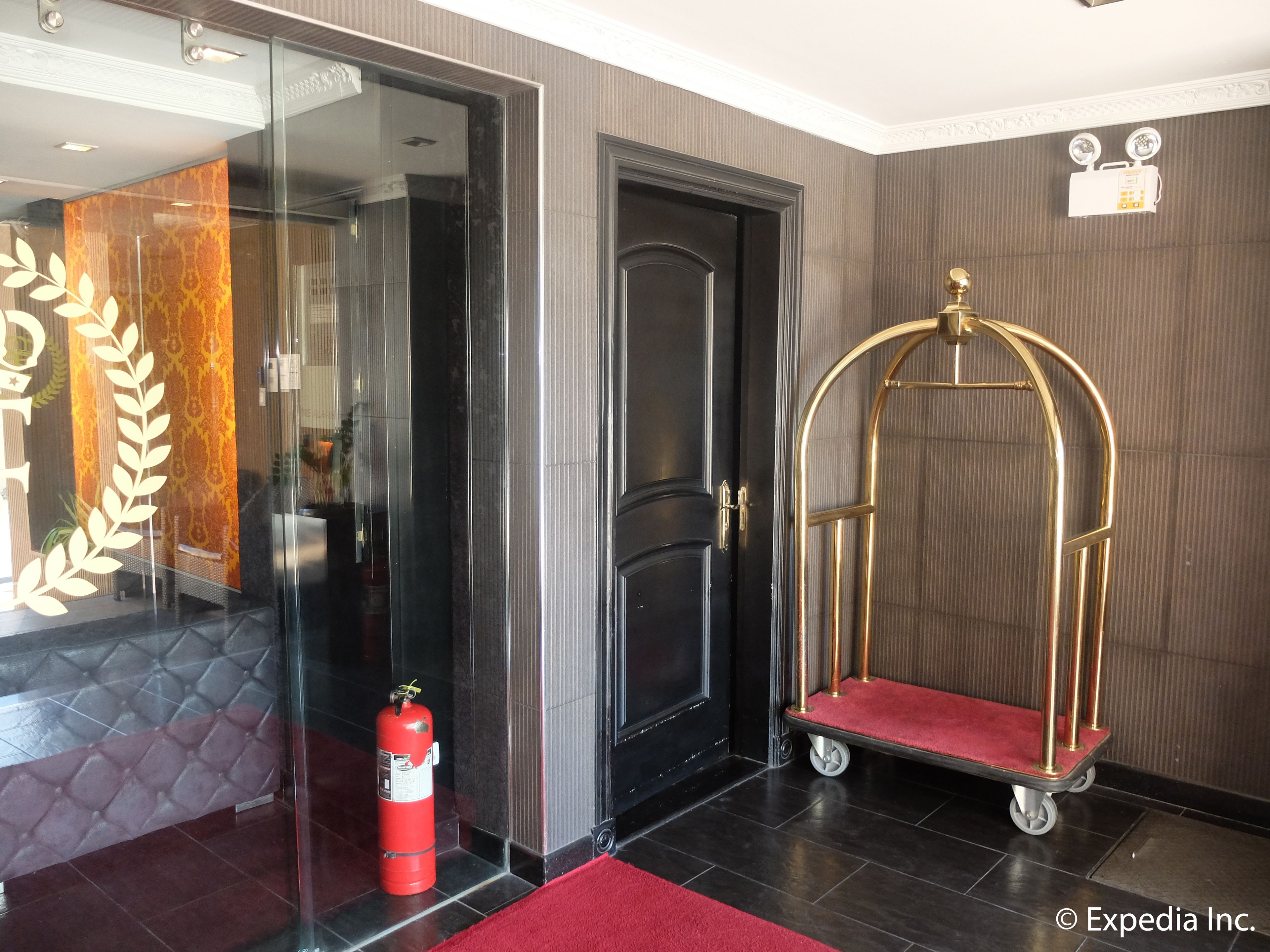 A hotel lobby with a glass door, a red fire extinguisher, and a gold luggage cart.