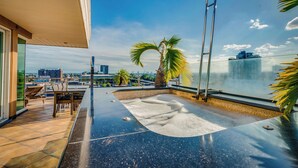 Una terraza en la azotea con piscina, sillones de descanso y vistas a la línea del horizonte de la ciudad y al agua.