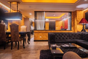 A modern living room with a black sofa, a dining table with chairs, and a large mirror reflecting the room.