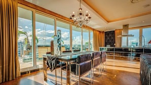 Un comedor amplio con una mesa y sillas de vidrio, un candelabro y vistas panorámicas de la ciudad a través de grandes ventanales.