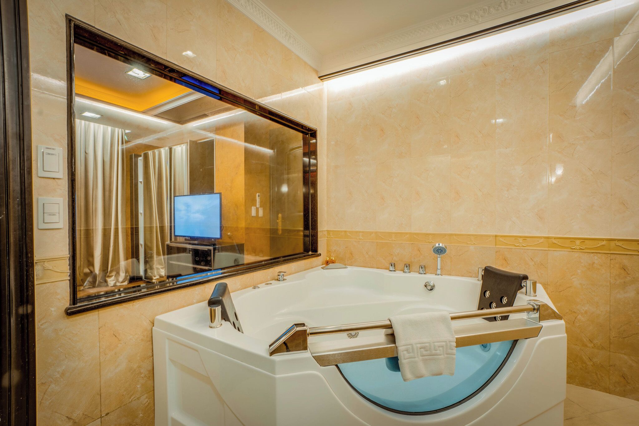 A modern bathroom with a large bathtub, a mirror, and a television in the background.