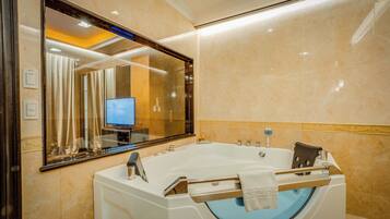 A modern bathroom with a large bathtub, a mirror, and a television in the background.