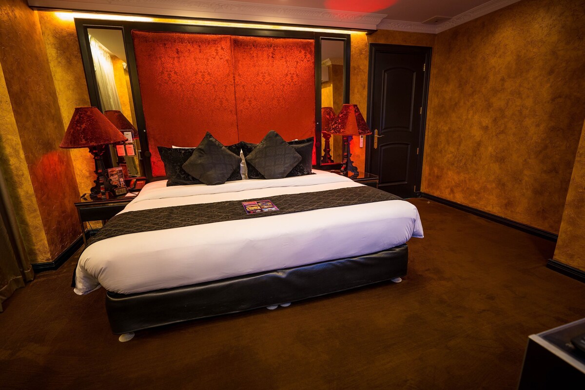 Una habitación de hotel con una cama grande, dos lámparas de noche, un espejo y una puerta.