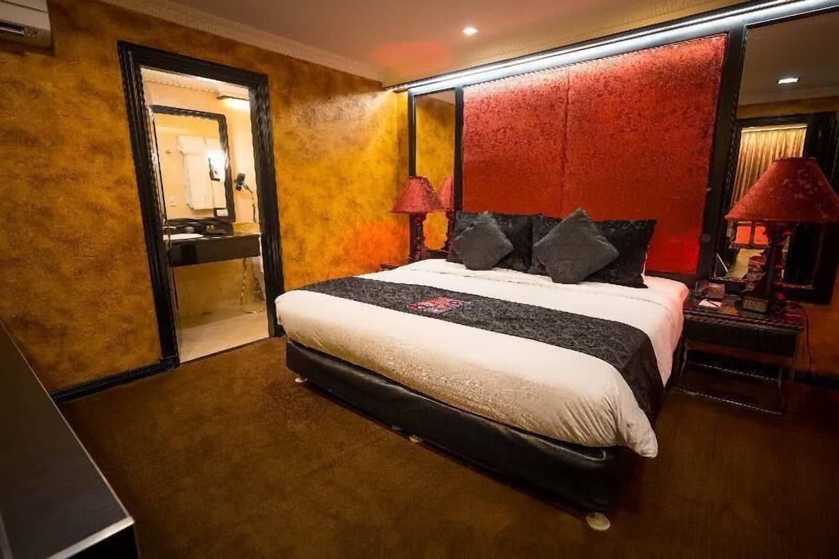 Hotellihuone, jossa on suuri sänky, yöpöytä lampun kanssa, peili ja ovi, joka johtaa kylpyhuoneeseen.
