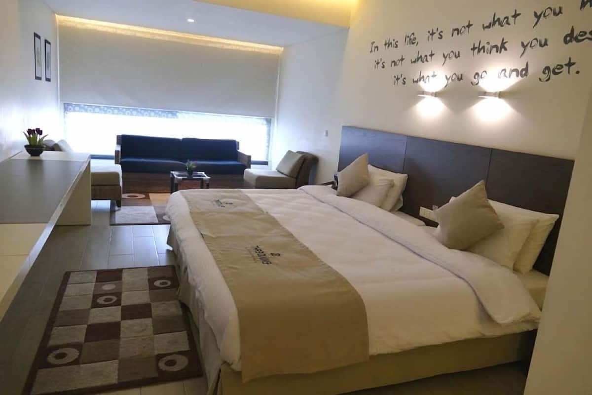 Una habitación de hotel moderna con una cama grande, un sofá, una mesita y una alfombra a cuadros.