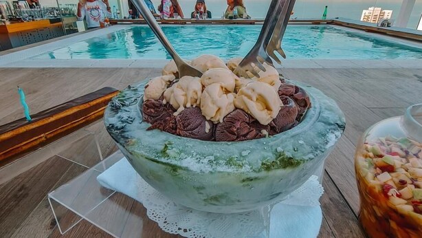 A poolside dining area with a large bowl of dessert, a glass of drink, and a view of the pool and guests. - Three ONine Urban House (Beirut)